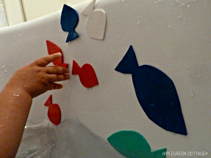 a toddler hand wet with water, grabbing a homemade craft foam fish while in a bathtub