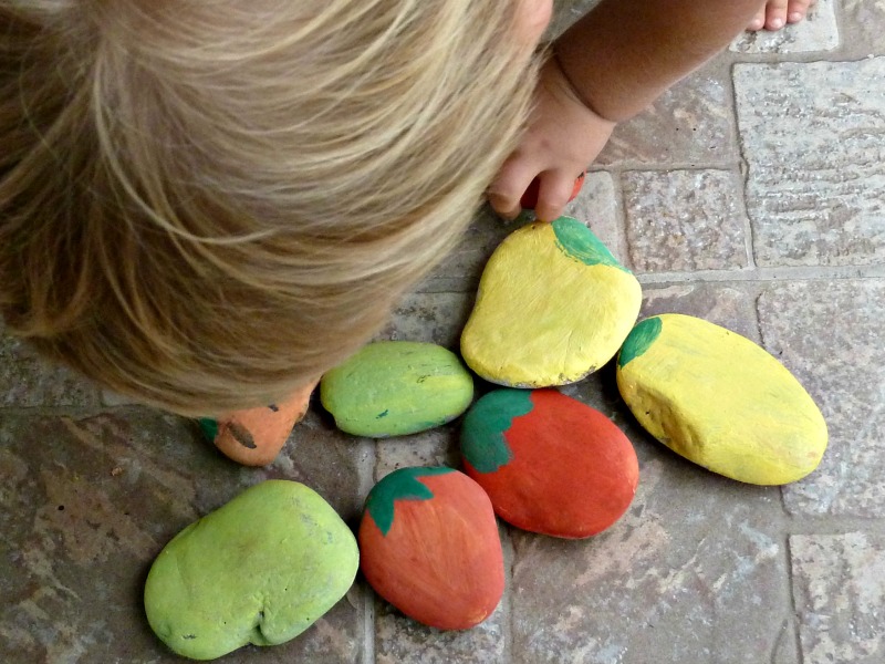 a person bent over a group of painted rocks for garden markers