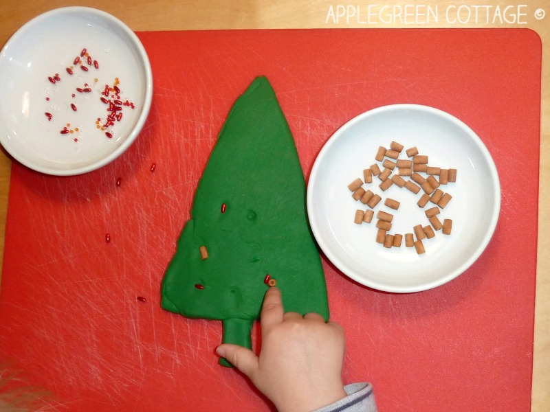 a toddler hand poking into a piece of green playdough next to other crafting materials