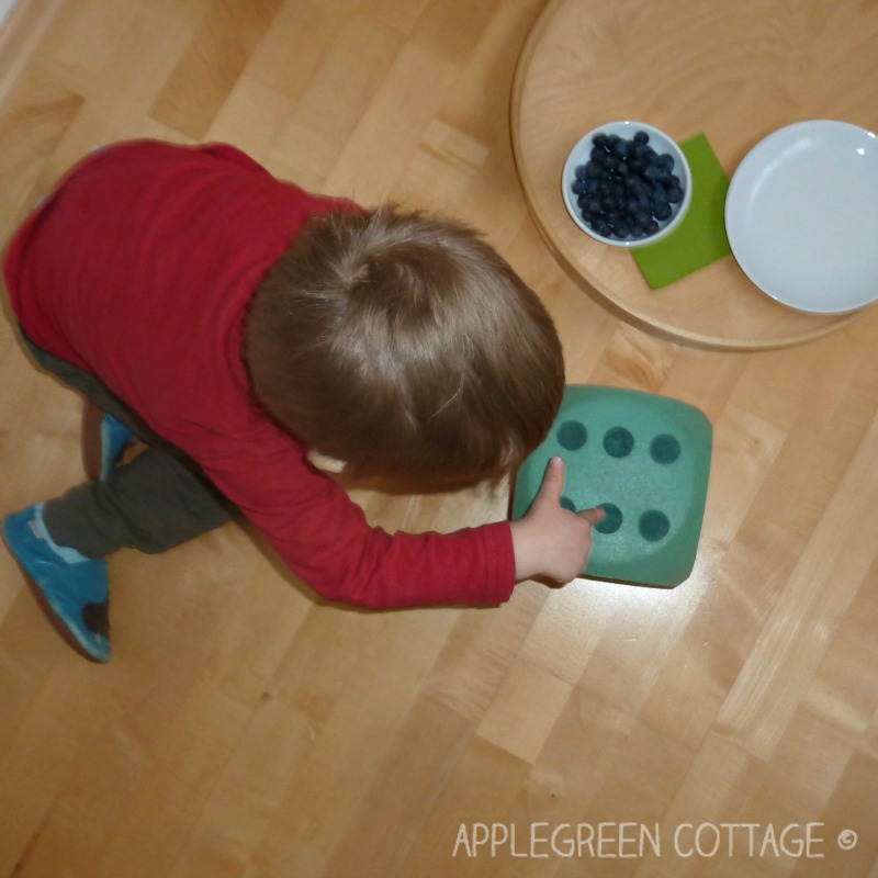 child playing with a large foam dice and a plate of blueberries