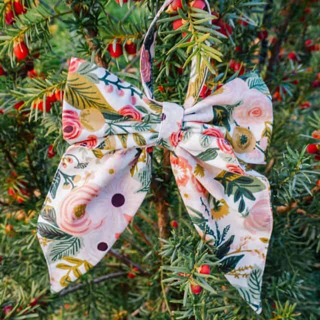 Fabric bow ornament hanging on a tree branch, showing simple folded construction for an easy sewing tutorial.
