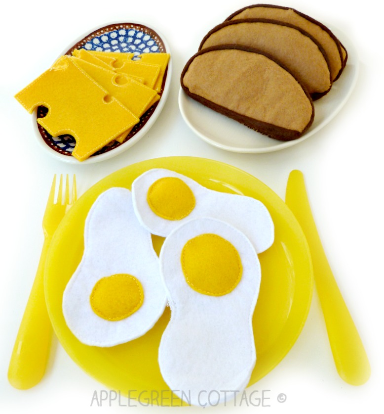 homemade playfood made out of felt: slices of cheese ona a blue and white ceramic plate, felt French bread slices, and three eggs sewn woth felt on a yellow plastic plate