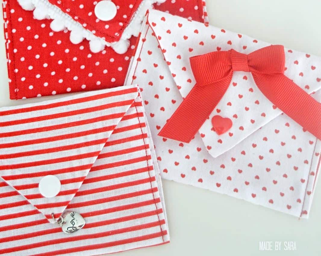 Here's a collection of 10+ adorable and easy Valentines sewing projects with links to free patterns and beginner sewing tutorials you just won't be able to resist. Sew up a few quick and easy Valentines gifts for your loved ones! Handmade fabric envelopes in vibrant red and white patterns, featuring stripes, polka dots, and small heart designs. Embellished with charming details like a bow, heart charm, and pom-pom trim, these envelopes are perfect for gifting or Valentine's Day.
