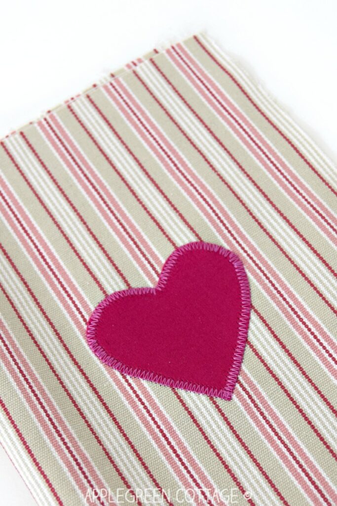 pink fabric heart applique sewn onto striped background fabric