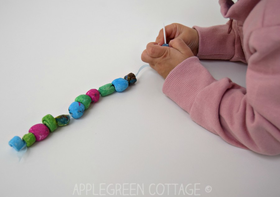 a kid threading diy clay beads into a diy bracelet