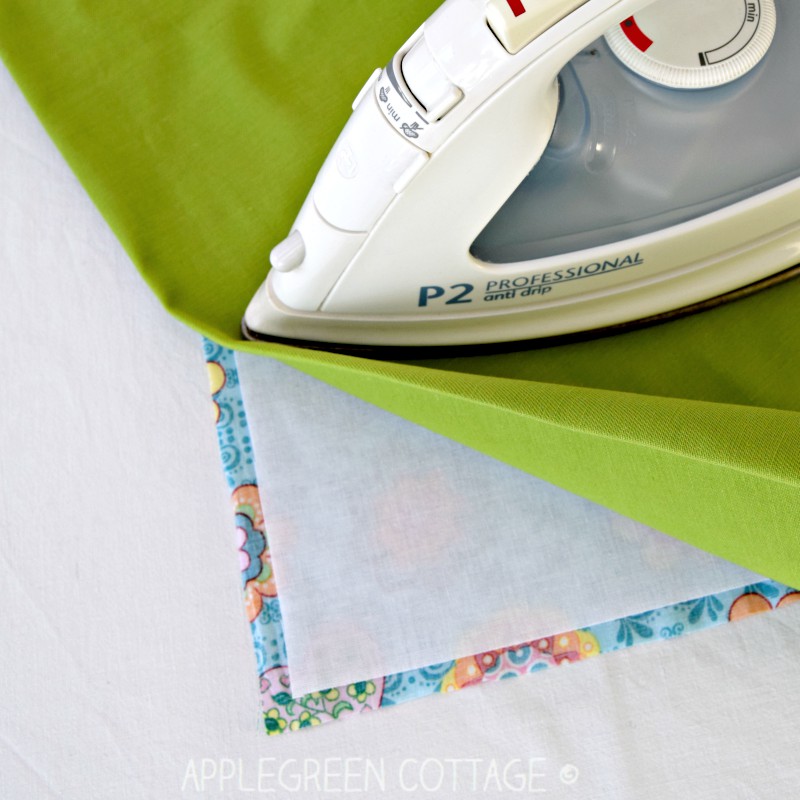 an iron pressing over a piece of green fabric and an interfaced printed fabric