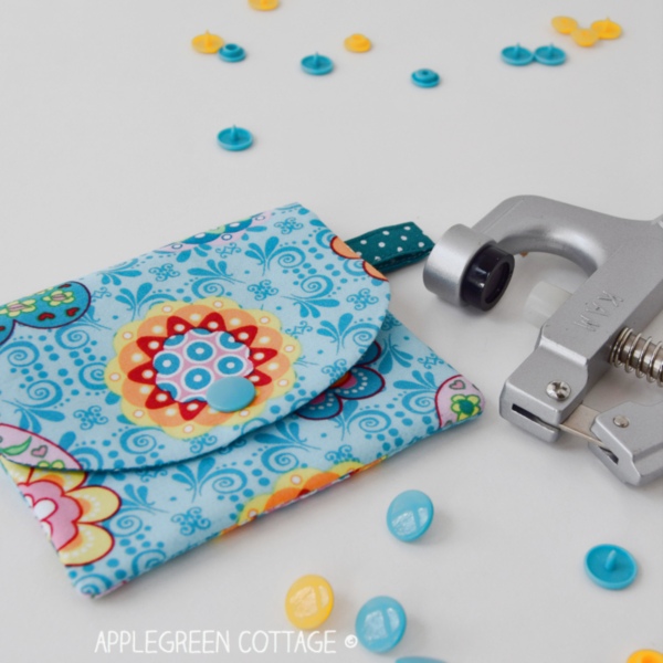 a blue printed fabric coin purse finished with a snap button, next to a kam snap set