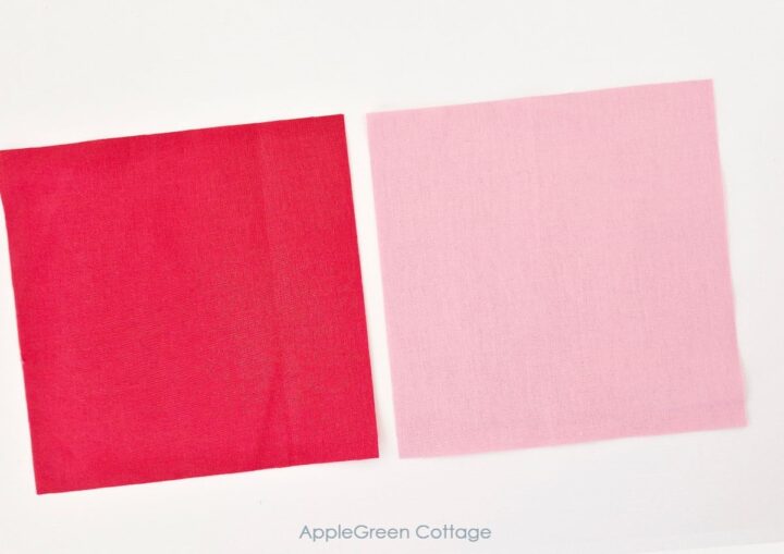 Close-up of red and pink fabric squares, showing two pieces of fabric for a four-patch quilt block.