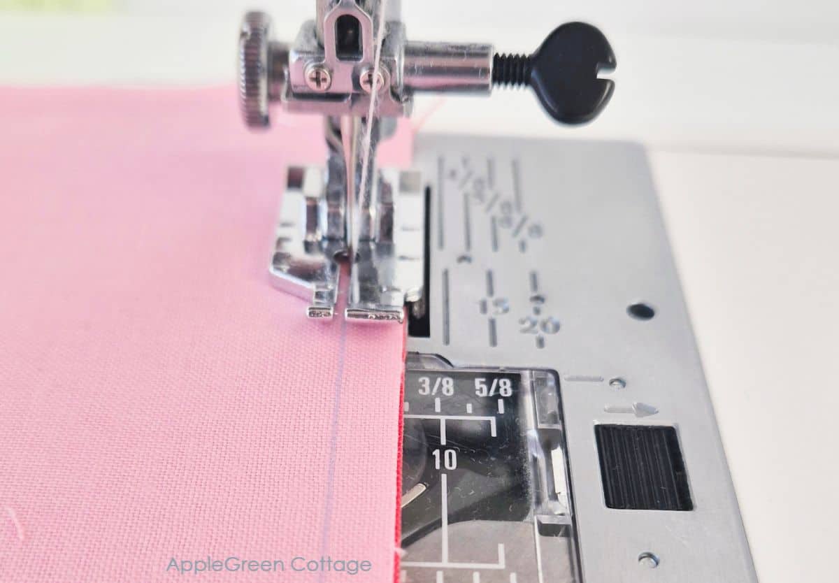 Sewing machine stitching along a pink fabric, demonstrating the process of quilting with a straight seam.