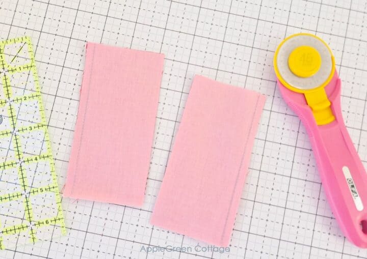 Two sewn fabric pieces of pink material aligned on a cutting mat, ready for trimming.