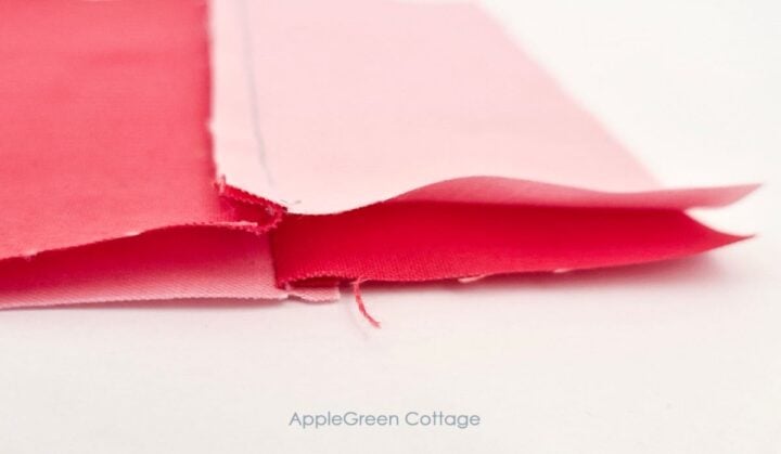 Two pink fabric pieces sewn together to form a two-piece unit of a four-patch quilt block, with a seam allowance visible.