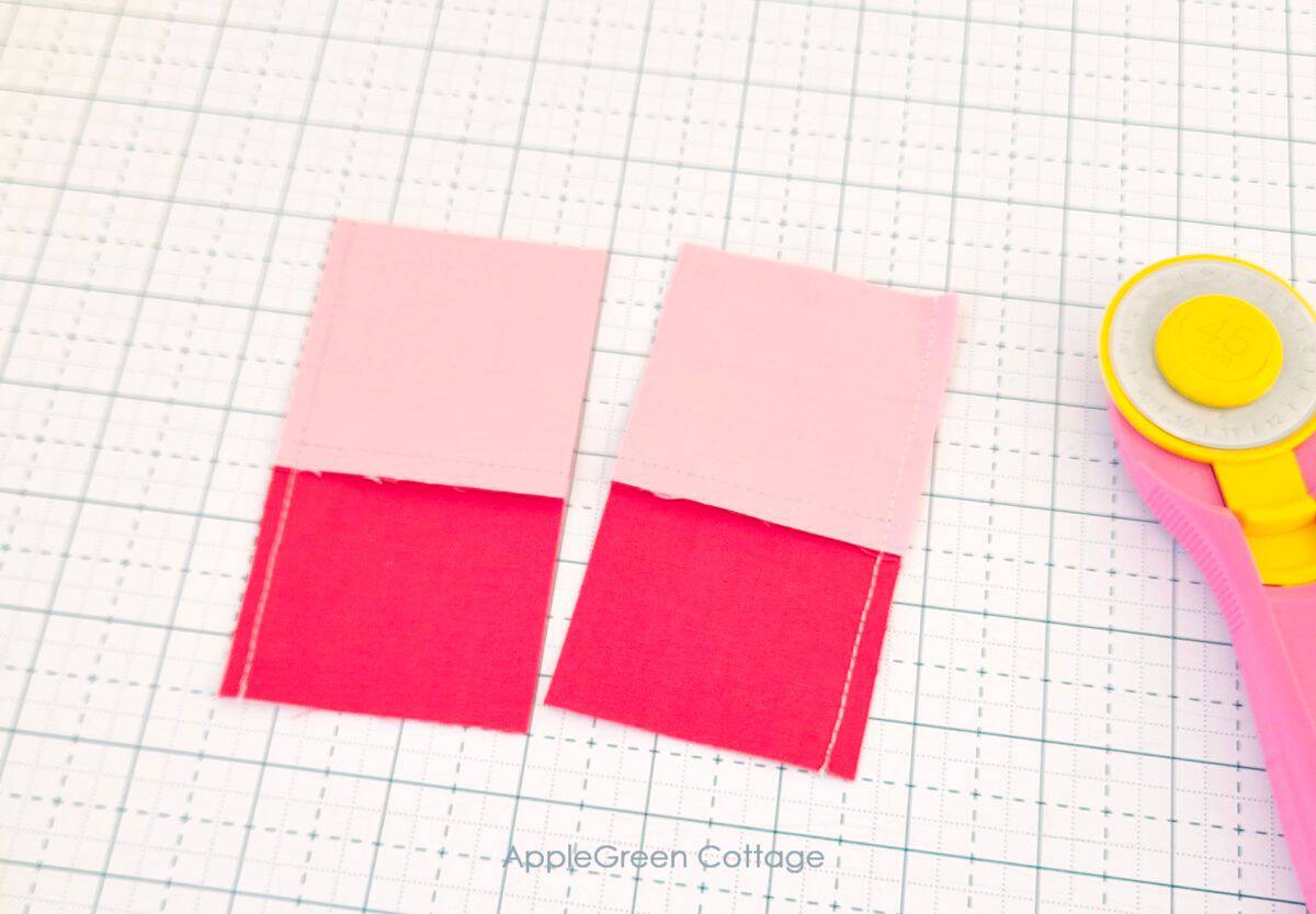 Two completed four-patch quilt blocks with pink and red fabric in a grid pattern on a white background.