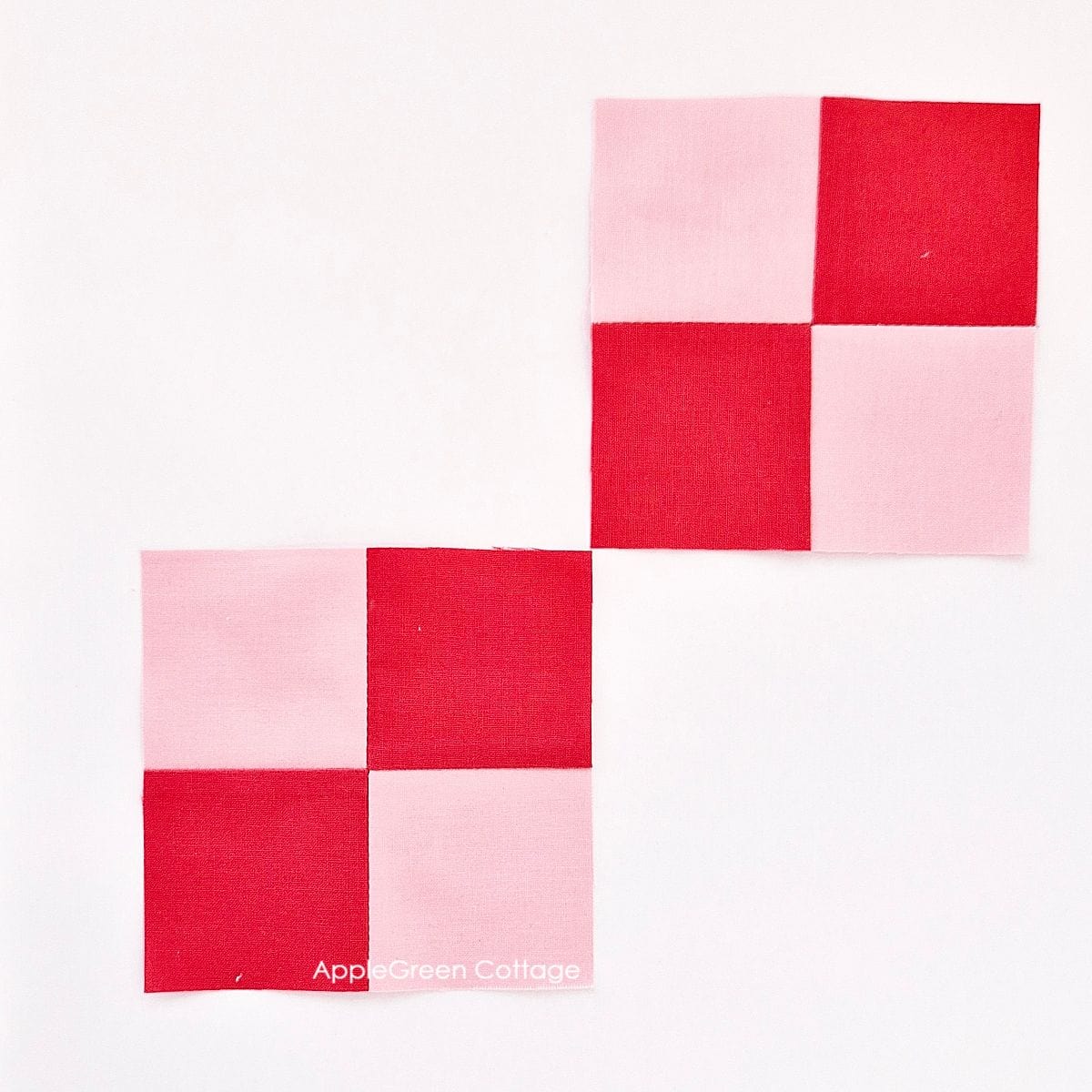 Two completed pink and red four-patch quilt blocks placed on a cutting mat, with a rotary cutter beside them.