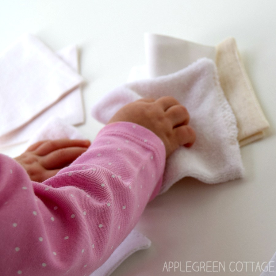 a set of white cloth squares that forms a travel game for babies, and a baby hand reaching for a piece