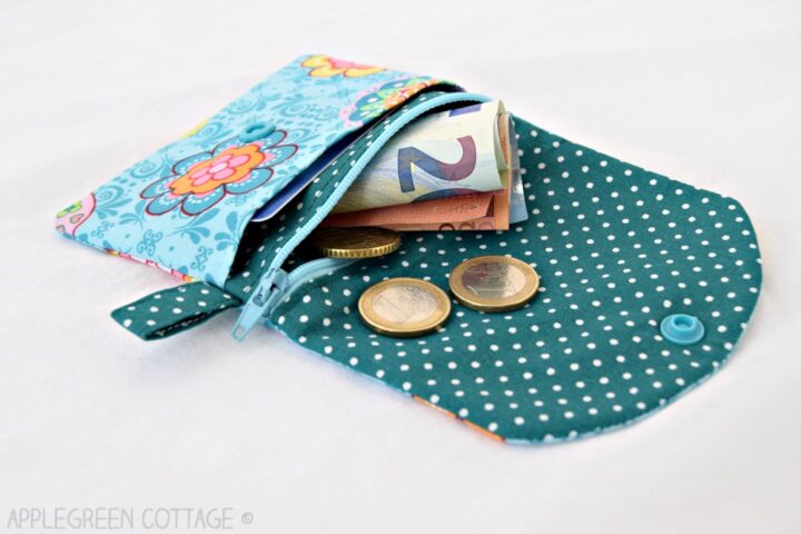 an open zipper pocket coin purse in polkadot teal fabric, with bills and coins peeking out