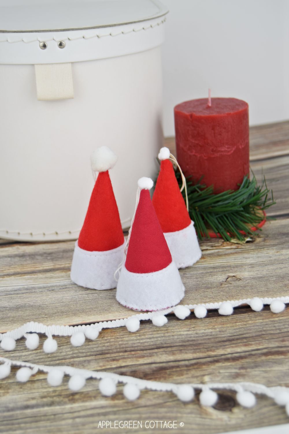 three finished santa hat ornaments placed next to a red candle on a christmass setting table