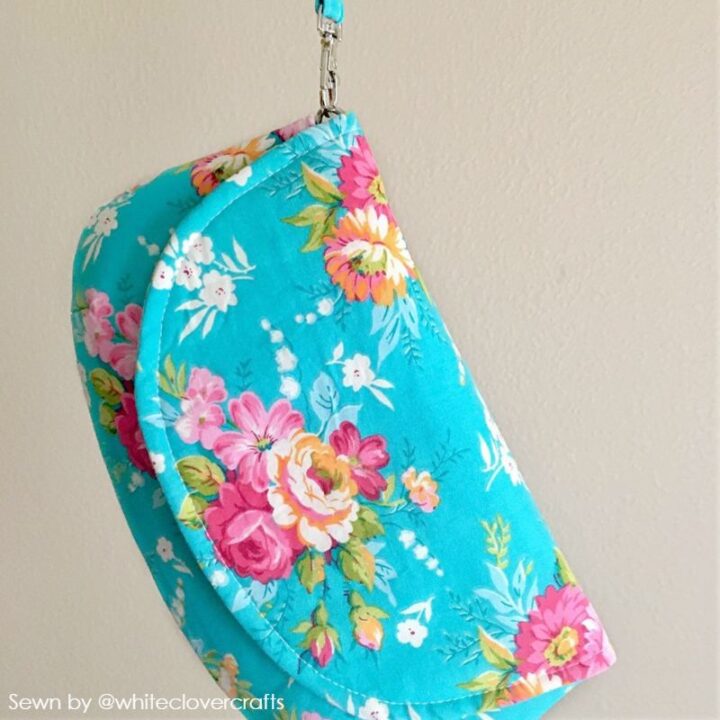 an elegant, small handmade fabric purse in blue floral cotton print with a flap and a wrist strap