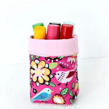 a finished small handmade fabric bin with coloring pencils stored in it and placed on a white table