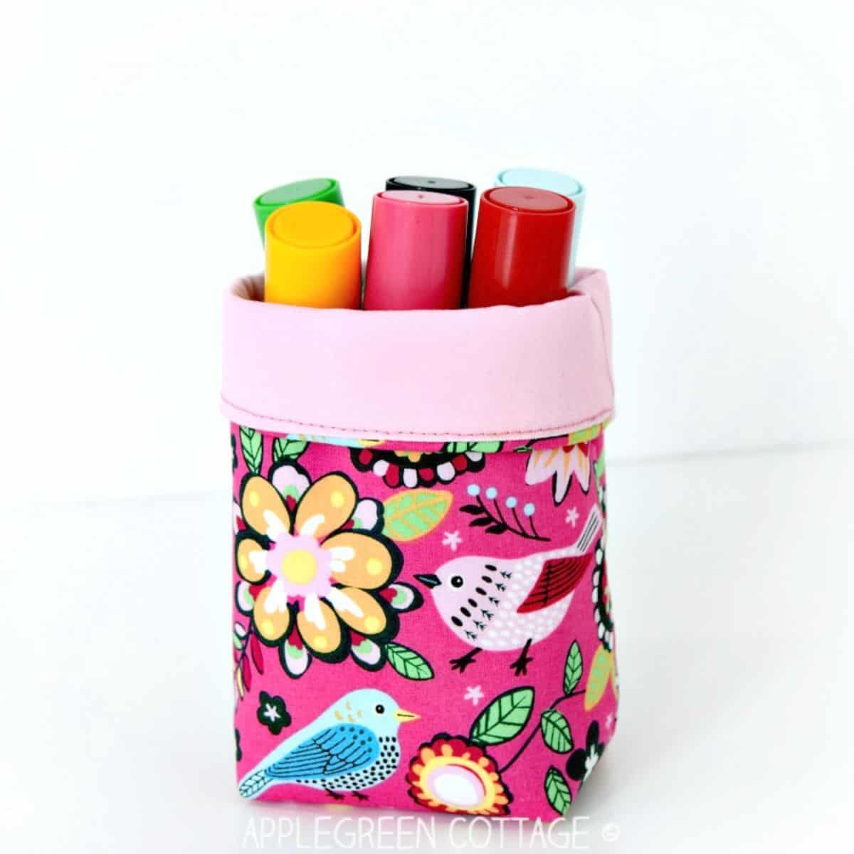 a finished small handmade fabric bin with coloring pencils stored in it and placed on a white table