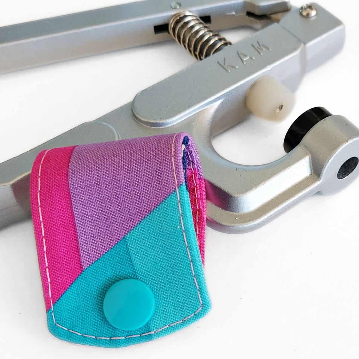 kam snap pliers behind a piece of fabric with installed plastic snap