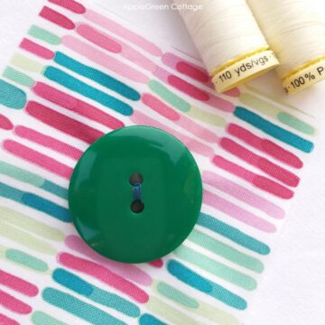 a green button sewn by hand on a piece of fabric