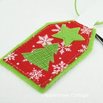 a fabric gift tag sewn with fabric scraps cut into smal star and tree pieces and stitched on a template