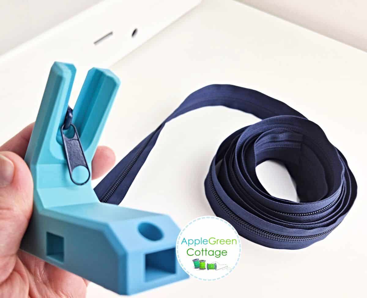 A blue plastic, 3-d printed zipper jig tool that you can attach to a tabletop, with a zipper slider on to add it to zipper tape.