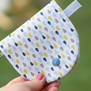 A hand holding a finished round-shaped coin purse in beautiful light quilting cotton, sewn with applegreencottage coin purse pattern.