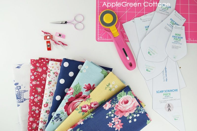 fat quarter bundle on a sewing table next to a rotary cutter by olfa, a pink cutting mat and some sewing notions