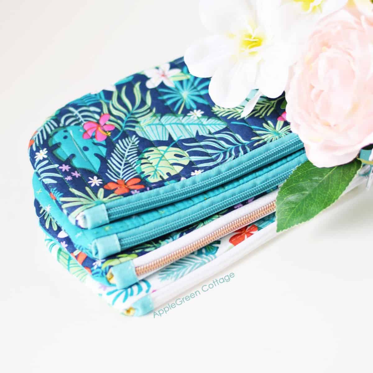 three finished quilted zipper pouches with a rounded bottom and a pieced exterior, in aqua blue and tropical prints