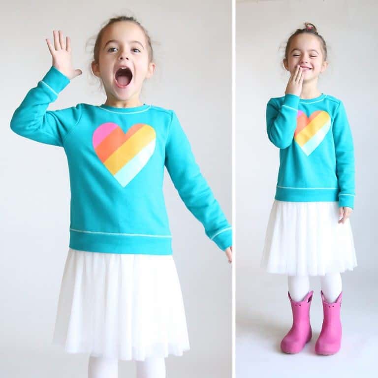 a girl in a teal and white homemade sweatshirt dress, jumping with joy and wearing pink rainboots