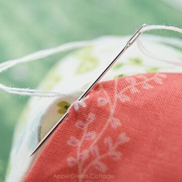 a hand sewing needle in a ladder-stitch position with white thread mending a hole in fabric