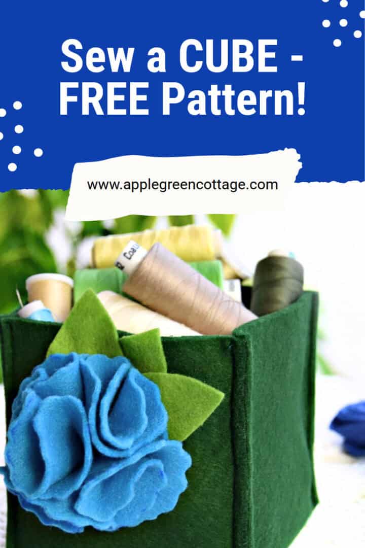 A finished green felt box with floral decoration on a tabletop, filled with thread spools and sewn with an applegreencottage pattern.