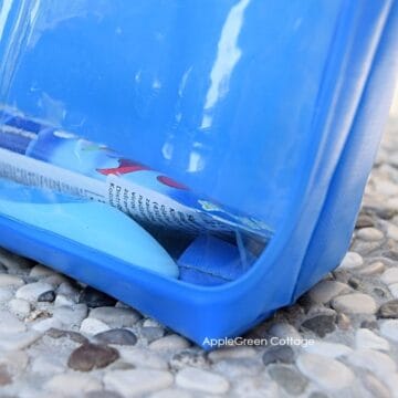 a finished handmade blue toiletry pouch with a transparent window, with toothpaste and a toothbrush, placed on pebbles