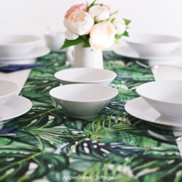 a finished handmade fabric table runner in green prints that was sewn with two layers and is reversible, in a table setting with white porcellain plates and cuttlery arranged on it