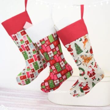 three finished christmas stockings in christmas cotton prints hanging on a pompom rope sewn with a free Christmas stocking pattern