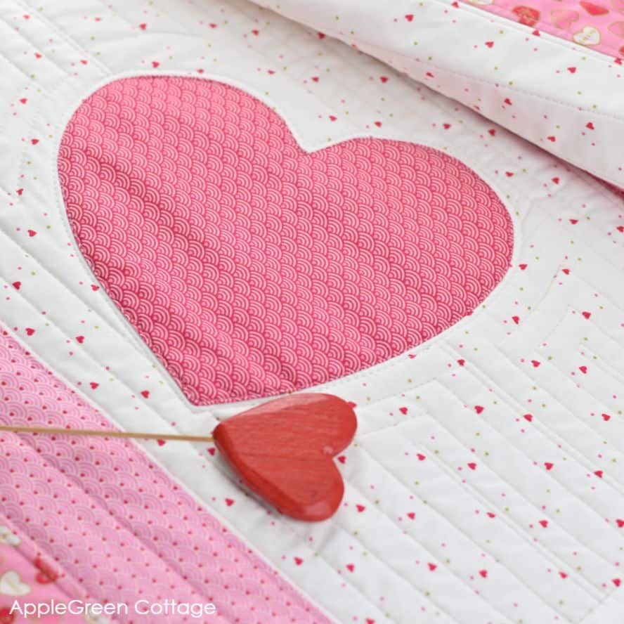 A close-up heart applique that is part of a quilted table runner with heart applique in pink, red, and white fabric.