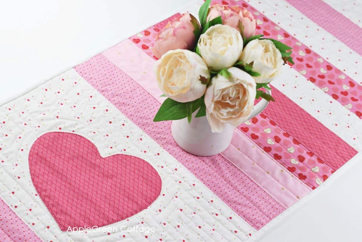 A finished homemade quilted table runner in a pink, red, and white color scheme, perfect for Valentine's Day or any romantic occasion.