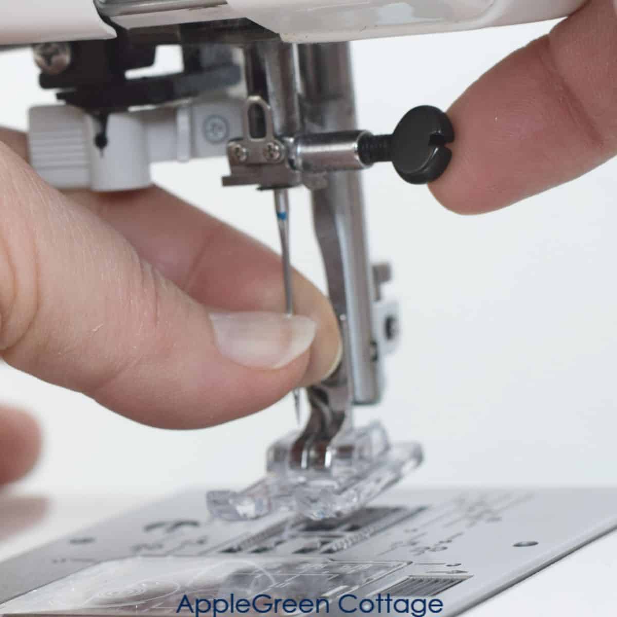 one hand holding a schmetz sewing machine needle in position in the needle holder on a sewing machine and the other hand turning the needle clamp to fix the needle shank into the sewing machine