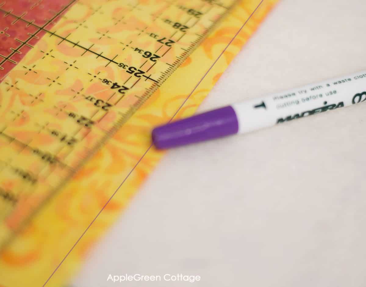 a quilting ruler on a piece of fabric with a marked stitching line next to an air erasable fabric marker