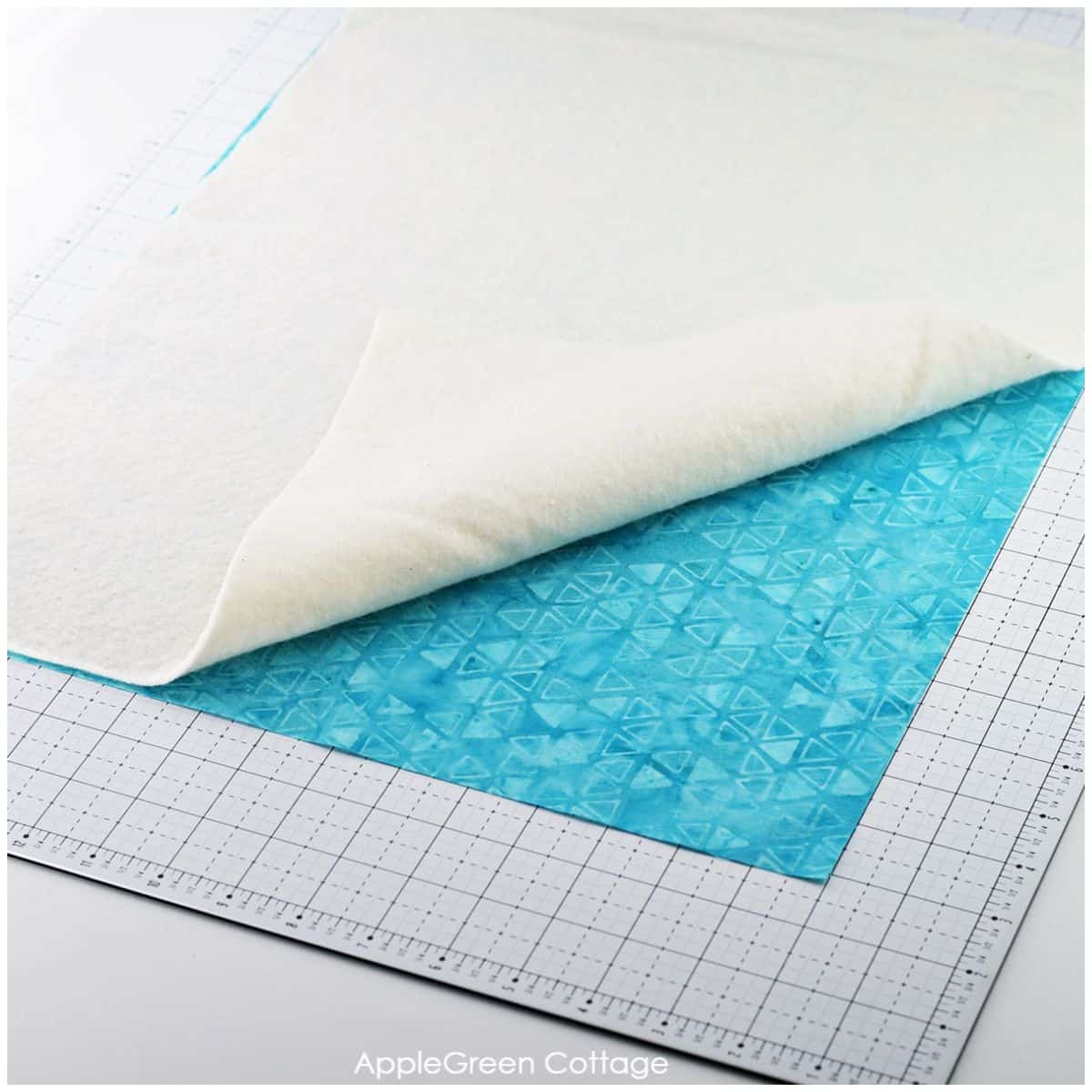 blue batik print backing fabric for a quilted placemat pattern covered by a piece of batting, on a fabric cutting mat