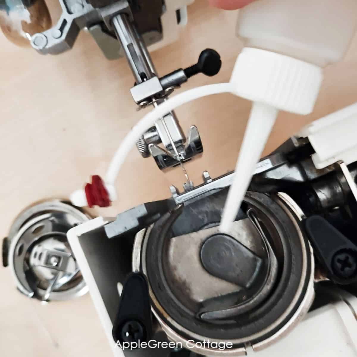 a closeup of a machine oil bottle tip is oiling a screw in the hook race compartment where the sewing machine bobbin is installed