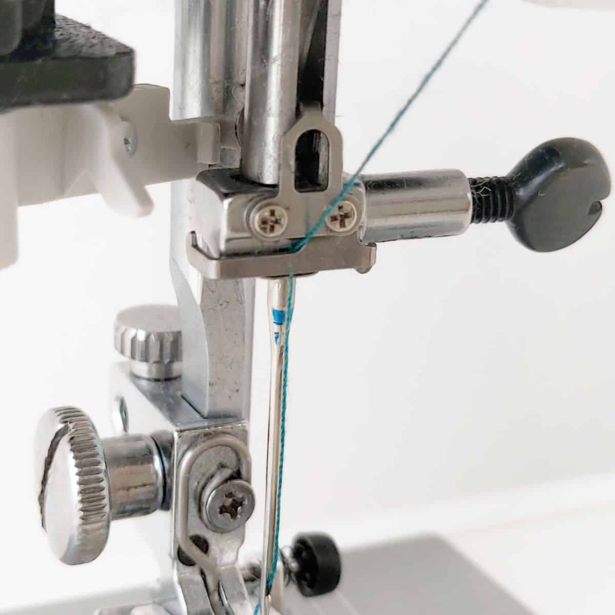 closeup of a sewing machine shank with a needle installed and showing a hook that holds the thread