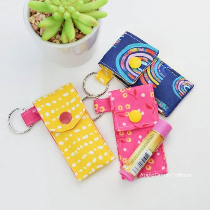 three finished yellow, blue, and pink fabric chapstick holders with snap closures next to a lip balm tube