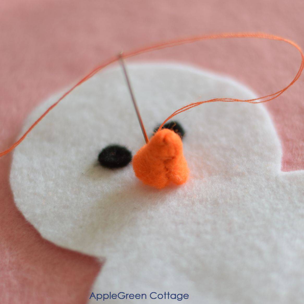 a tiny orange scone made out of felt being attached to the middle of a felt snowman's head