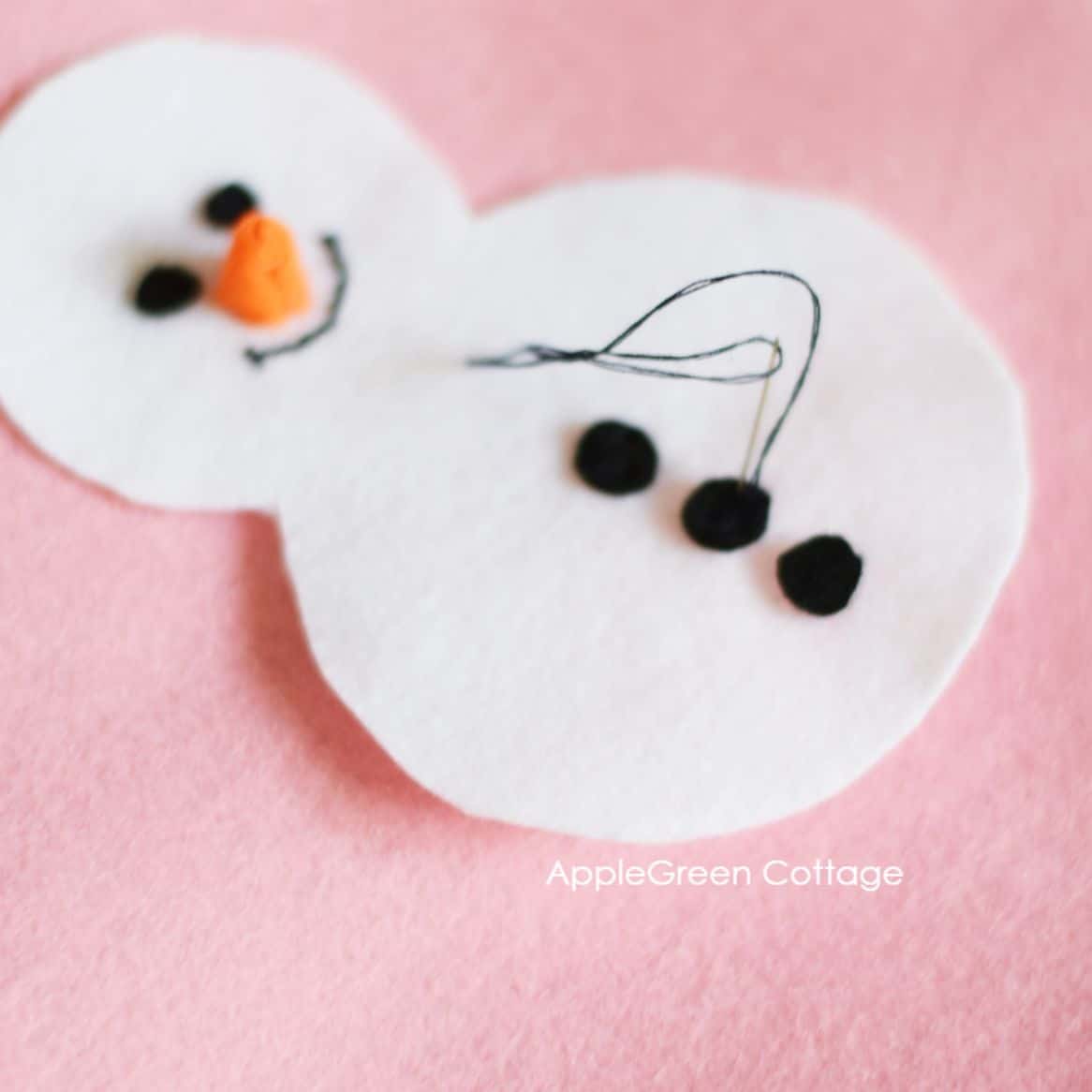 black thread and needle peeking out of a black felt button on a snowman form