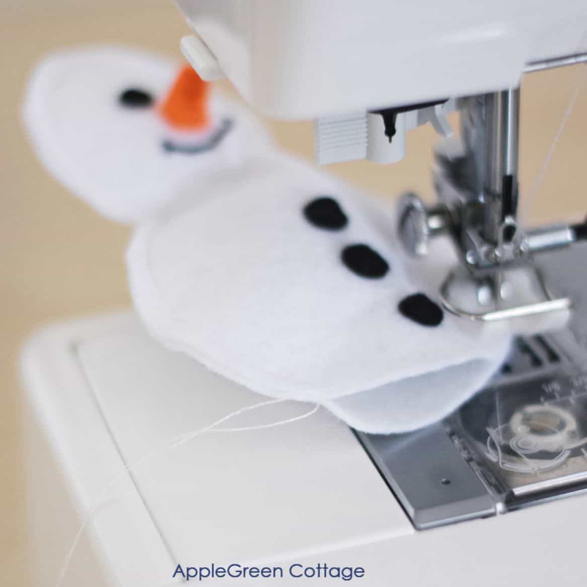 closeup of a sewing machine sewing two felt snowman layers together