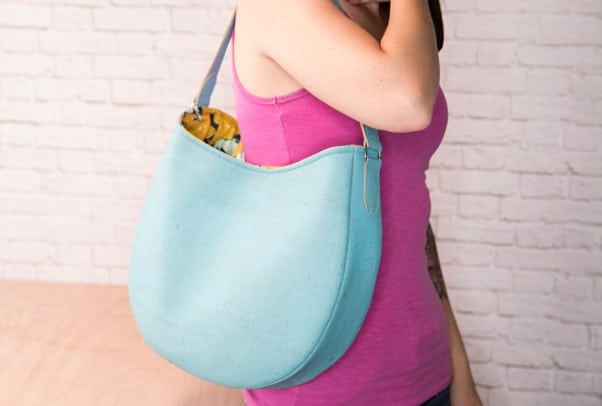 a woman in a pink tank top carrying a faux leather blue round hobo bag