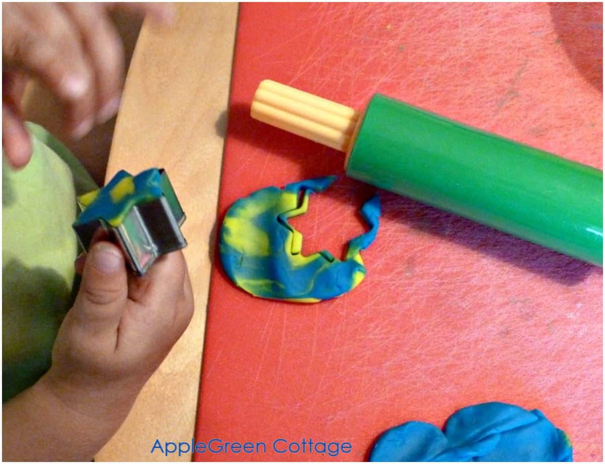 toddler's hand using a cookie cutter to create with playdough