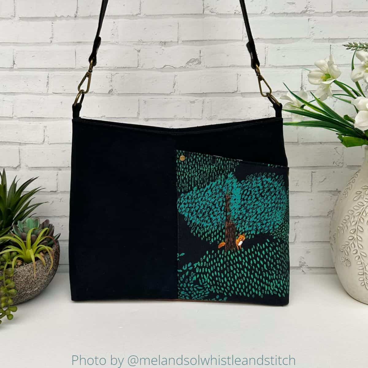 a handmade bag with a front exterior pocket, sewn with black canvas and a beautiful designer cotton print, and a brown leather bottom